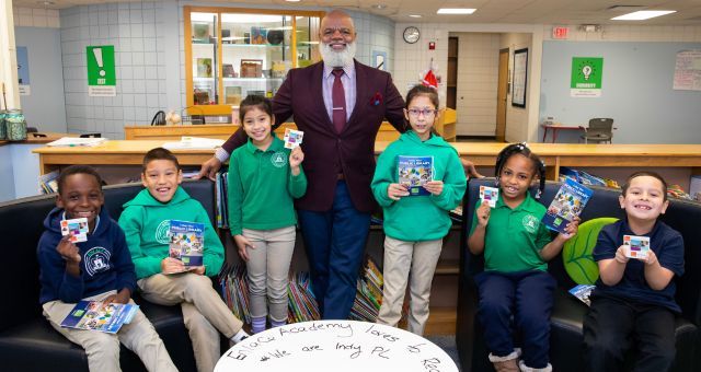 Indianapolis Public Library CEO Gregory Hill poses with six smiling elementary students who are holding their new library cards.
