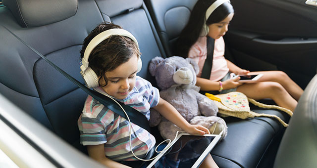 Kids listening to headphones and using mobile devices while riding in a car.