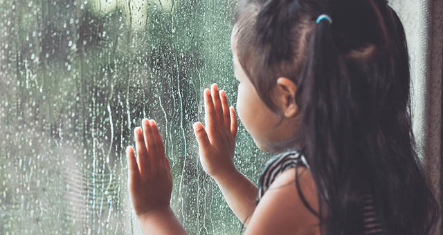 Child looking out a window at the rain.