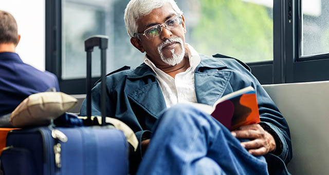 Man reading sitting next to luggage.