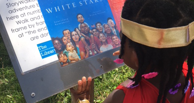 Child reading a story page at one of the storywalk stations.