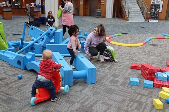 Two small children and an adult playing on life-size Tinker Toys on the floor of Central Library.