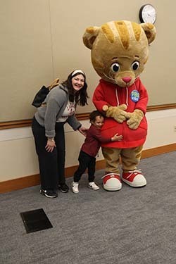 A small child hugs Daniel the Tiger while getting a picture taken.