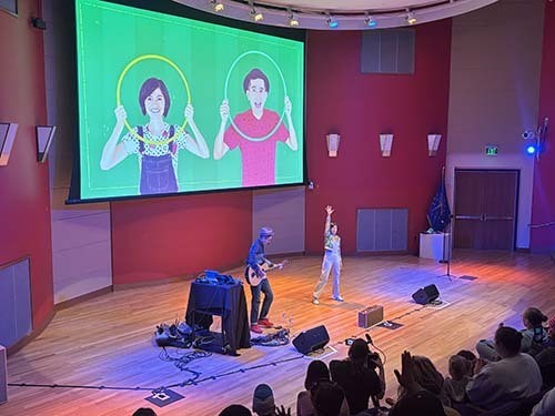 Two musicians lead the singing in an auditorium full of children and their families.