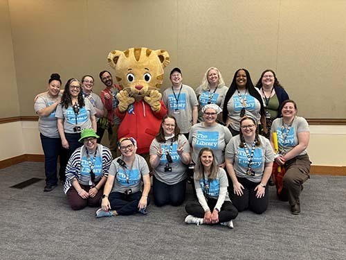 A large group of Library staff gather around Daniel Tiger for a photo..