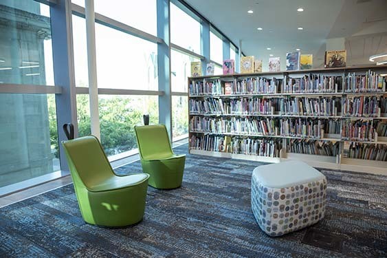 Two soft green chairs in front of floor to ceiling windows near the Kid Central book stacks.