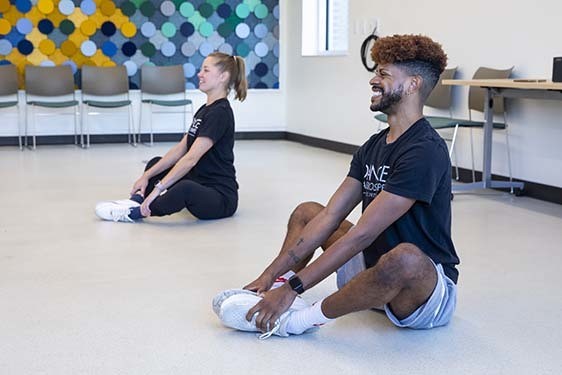Two dance instructors sitting on the floor demonstrating a dance move.