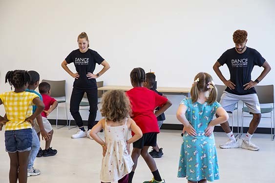 Group of children following teachers in front of the group demonstrating dance moves.
