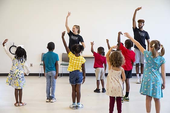 Group of children following teachers in front of the group demonstrating dance moves.