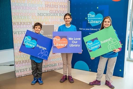 Three kids with We Love Our Library signs.